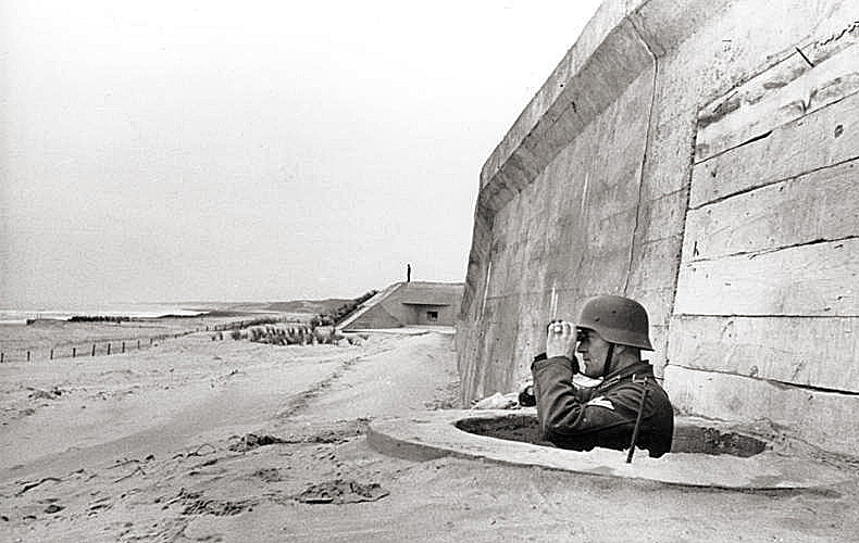 The unending watch along the Atlantic Wall as a German soldier gazes seaward through binoculars.