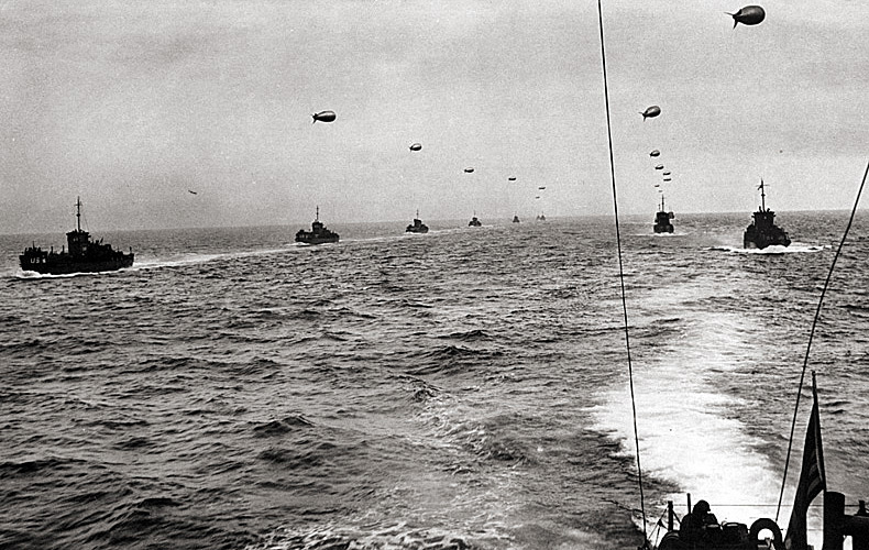 A large convoy of Landing Craft Infantry sails across the English Channel toward the Normandy invasion beaches. Each landing craft tows a barrage balloon to protect against low-flying German fighters.