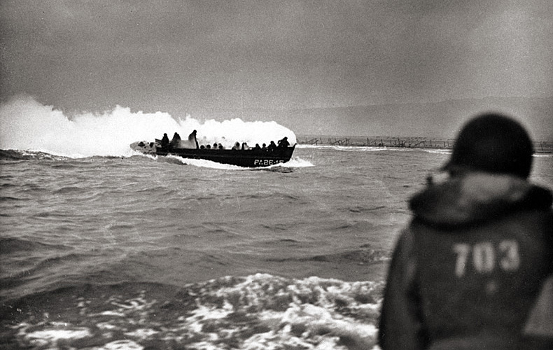 A landing craft approaches the beach smoking from a fire caused by a German machine-gun bullet striking a hand grenade. After landing the troops, the boat's crew put out the fire and returned to their transport.