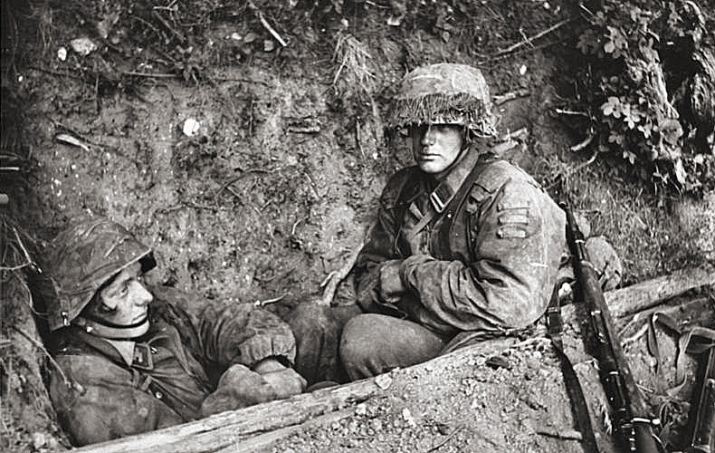 Worn out-looking German Panzer troops in a foxhole await whatever will come next.
