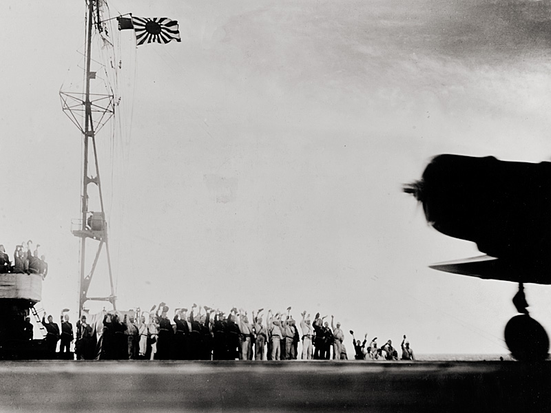 A Japanese Navy Type 97 Carrier Attack Plane (Kate) takes off from a carrier as the ship's crewmen shout the battle cry, “Banzai.”