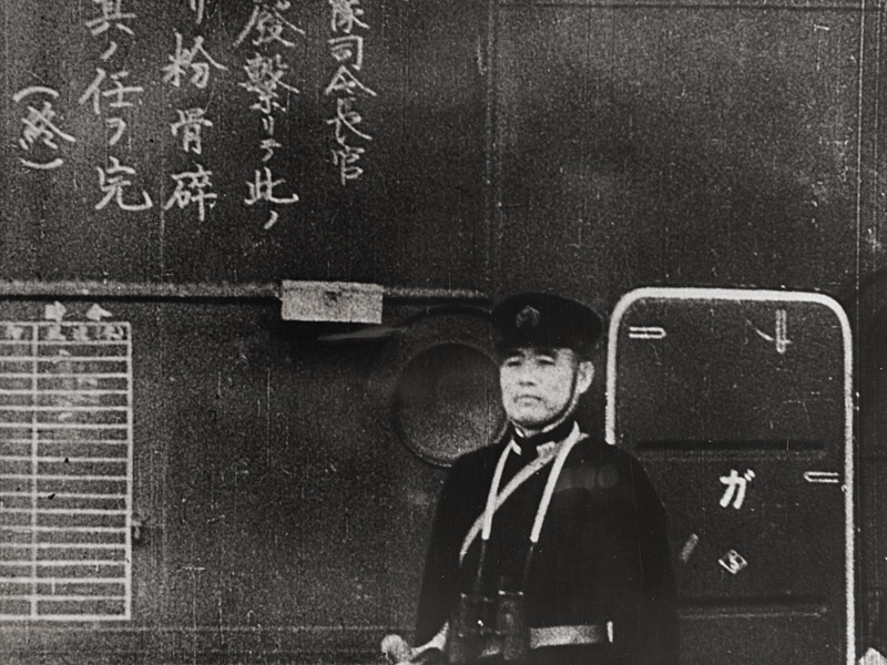 Commanding Officer of the Japanese aircraft carrier Shokaku watches planes take off to attack Pearl Harbor. The Kanji inscription at left tells pilots to do their duty.