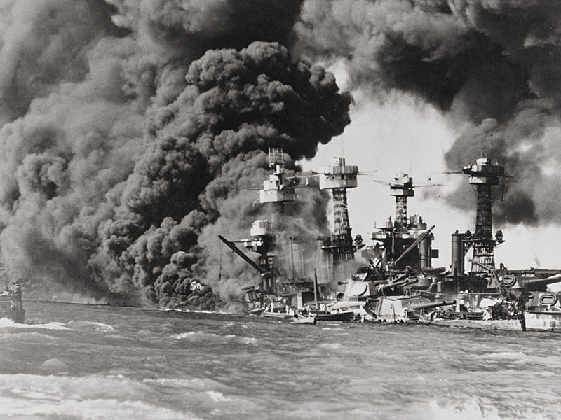 USS West Virginia aflame, with USS Tennessee seen on the sunken  battleship's far side. 