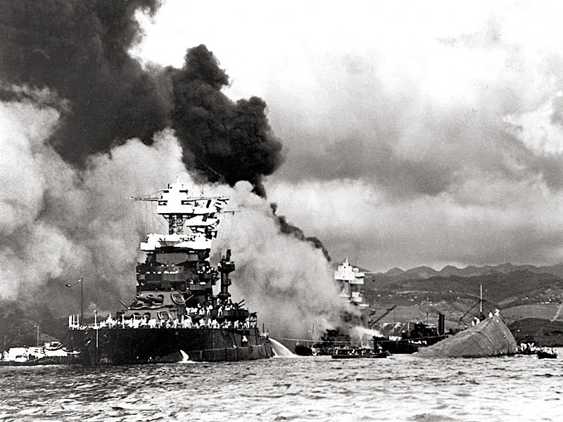 USS Maryland alongside the capsized USS Oklahoma. USS West Virginia is burning in the background.
