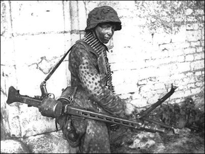 A young machine-gunner totes an MG-42 at Caen in northern France shortly after D-Day.