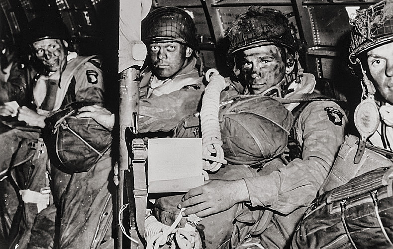 The determined faces of American paratroopers about to take off for the very first D-Day assaults. The paratrooper in the foreground holds a copy of General Eisenhower's message of good luck and clasps his bazooka in anticipation.


