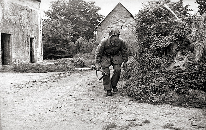 A German infantryman moves into position behind thick bushes.