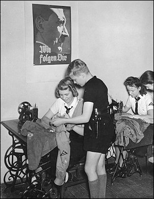 Inside a sewing room of the BDM in 1942 as Hitler Youth uniforms are brought in to be mended. On the wall hangs a portrait of Hitler saying: "We follow Thee." 